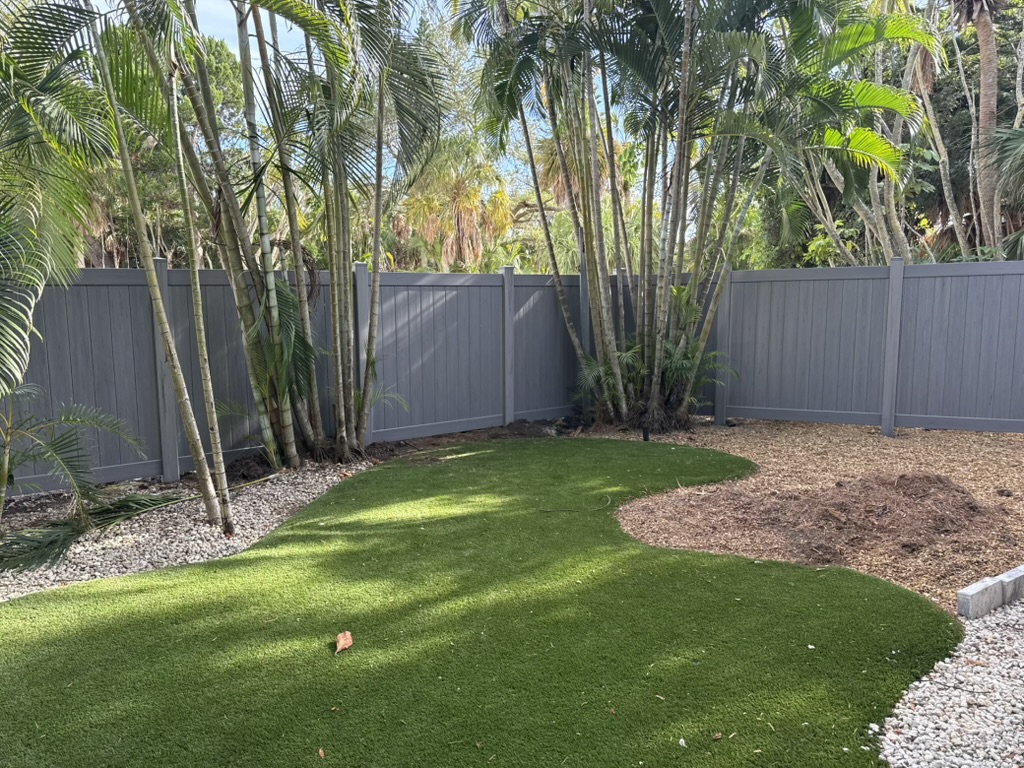 Gray vinyl privacy fence framing a backyard turf lawn
